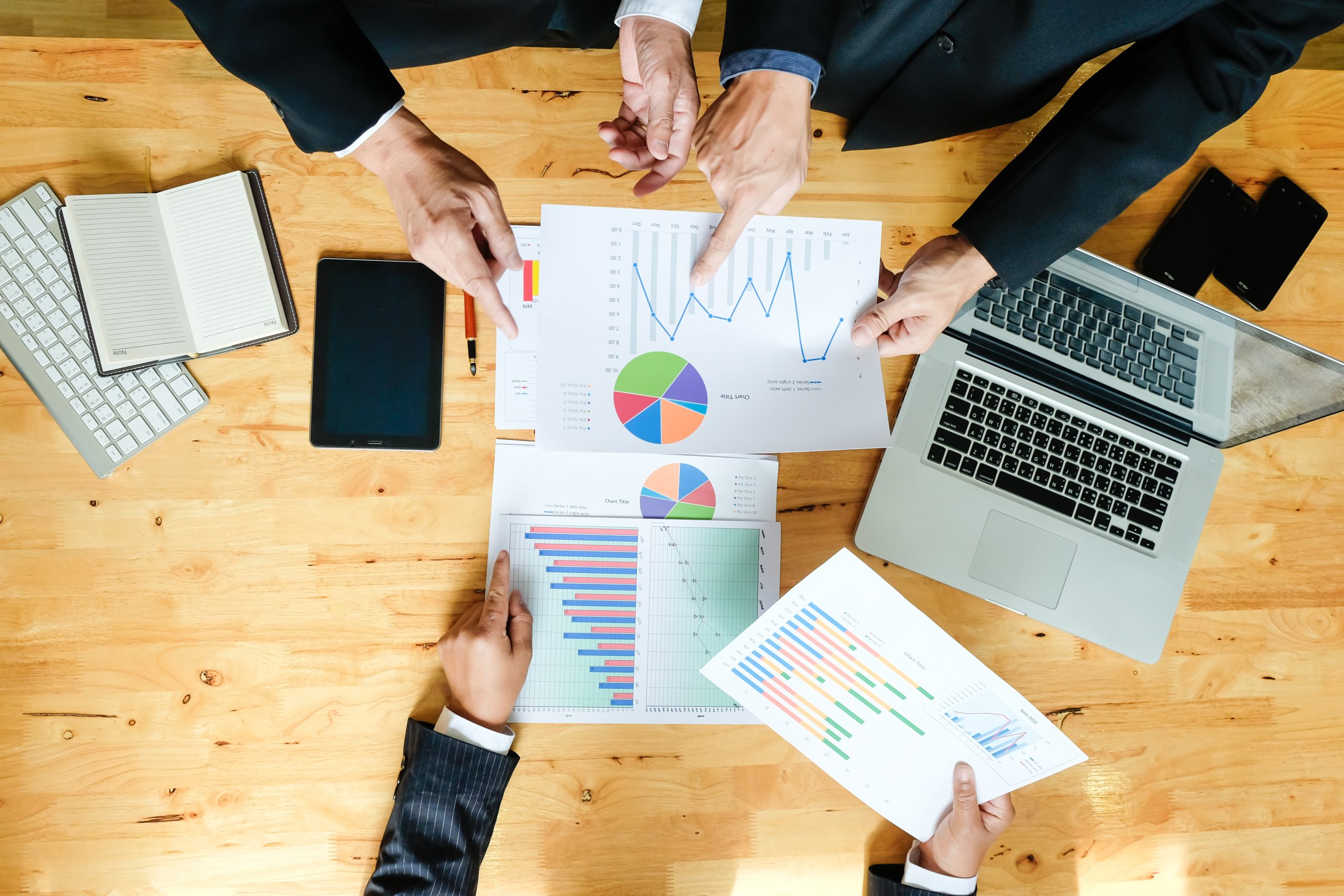 Close-up of a team discussing performance graphs and business reports on paper during an OKR implementation meeting in the UAE, with hands pointing to key data for strategic planning and goal alignment.