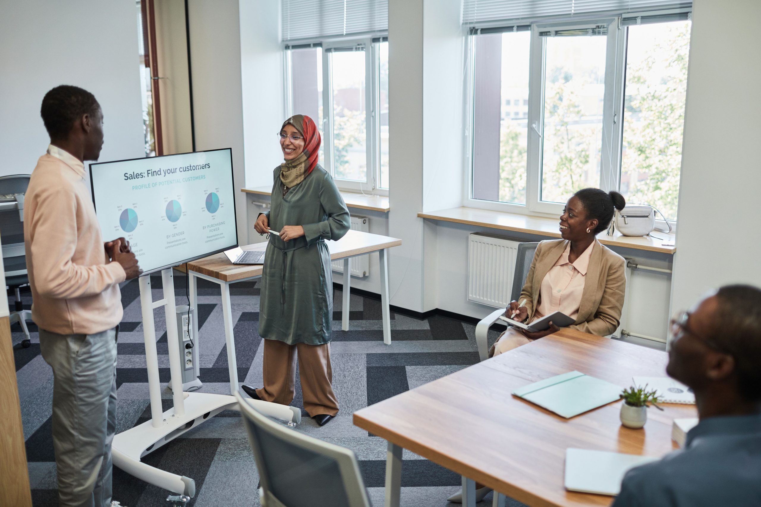 Female sales coach standing in front of a whiteboard with a marker, delivering sales training and coaching to a team of professionals during a corporate workshop.