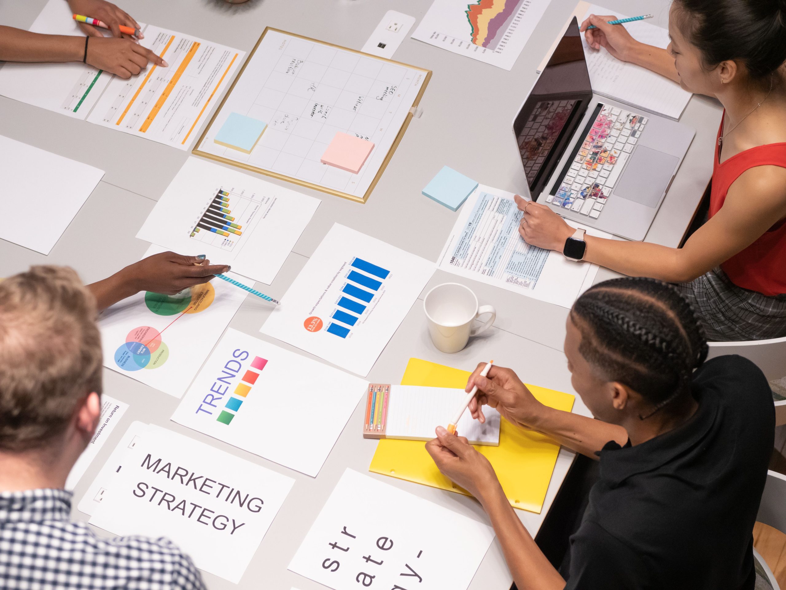 Team collaborating on marketing collateral design strategy with reports, graphs, and branding documents spread across a meeting table.
