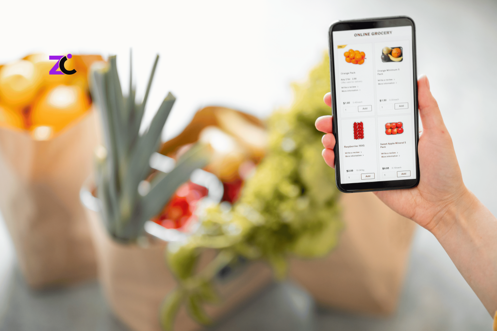 Online Grocery Store Development showcasing a woman using a grocery shopping app on her mobile phone with fresh groceries displayed in the kitchen