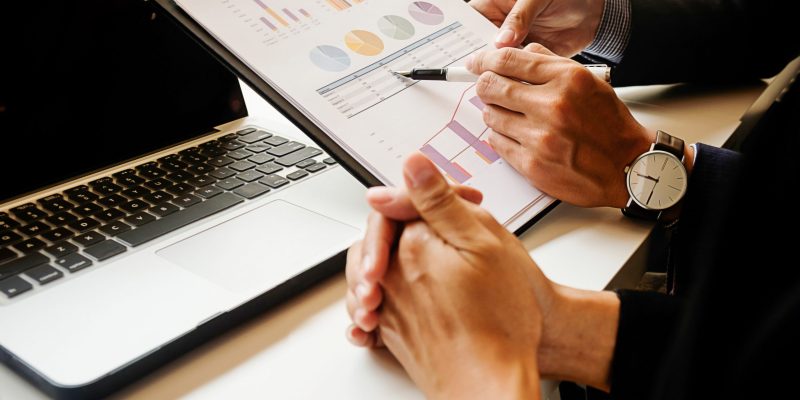 Close-up of two employees reviewing performance graphs during an OKR implementation meeting in the UAE, with one person presenting printed charts while the other holds a pen and discusses business objectives and progress.