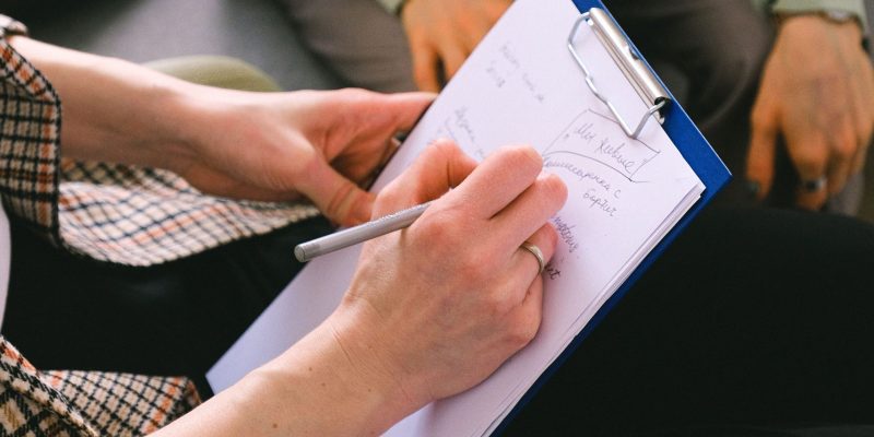 Female professional reviewing a document and writing notes with a pen, representing Job Evaluation & Grading Services through role assessment, job analysis, and structured workforce framework development.